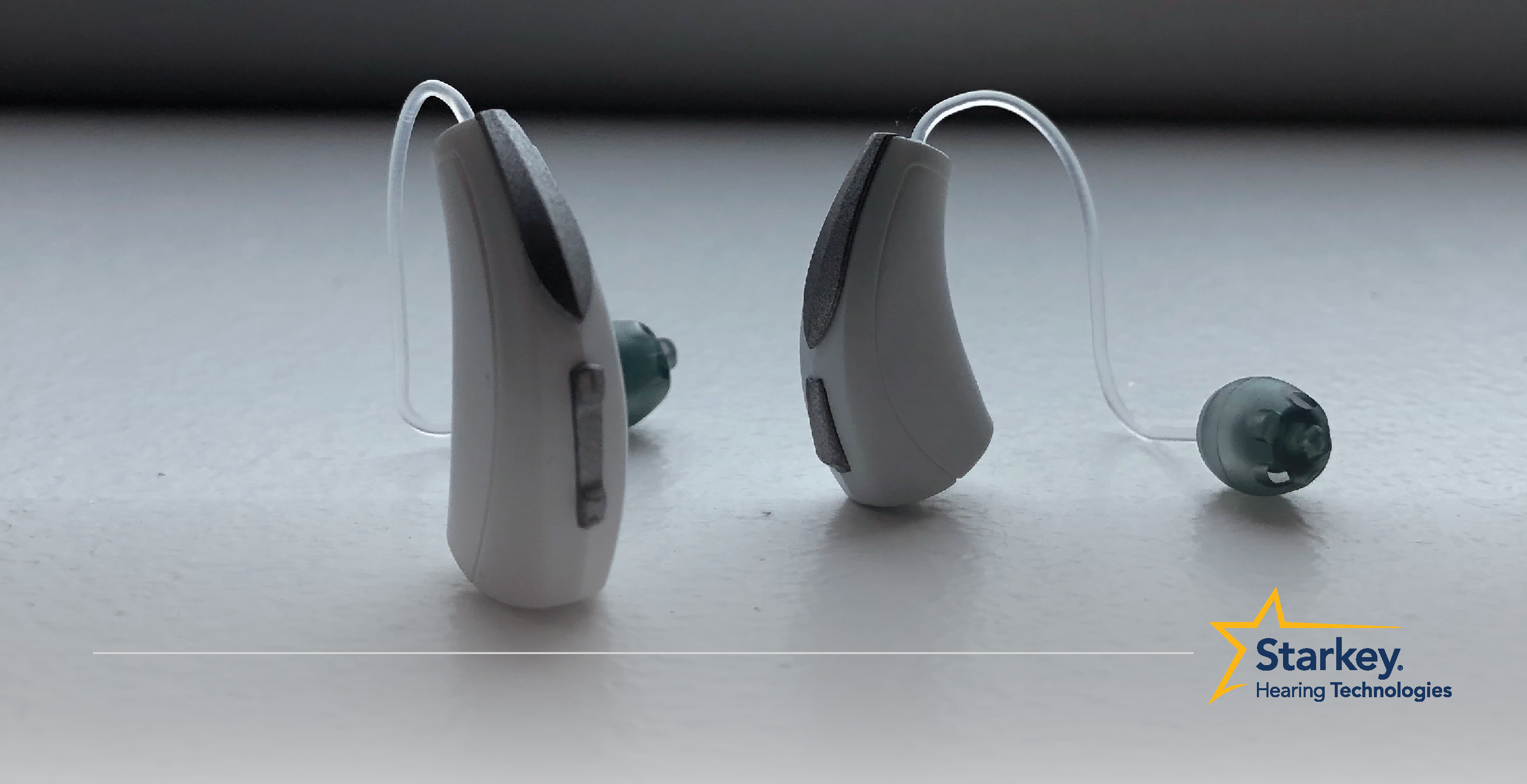 Aide auditive récepteur-dans-canal blanche directement à côté d'une aide auditive mini récepteur-dans-canal tournée sur le côté sur une surface blanche
